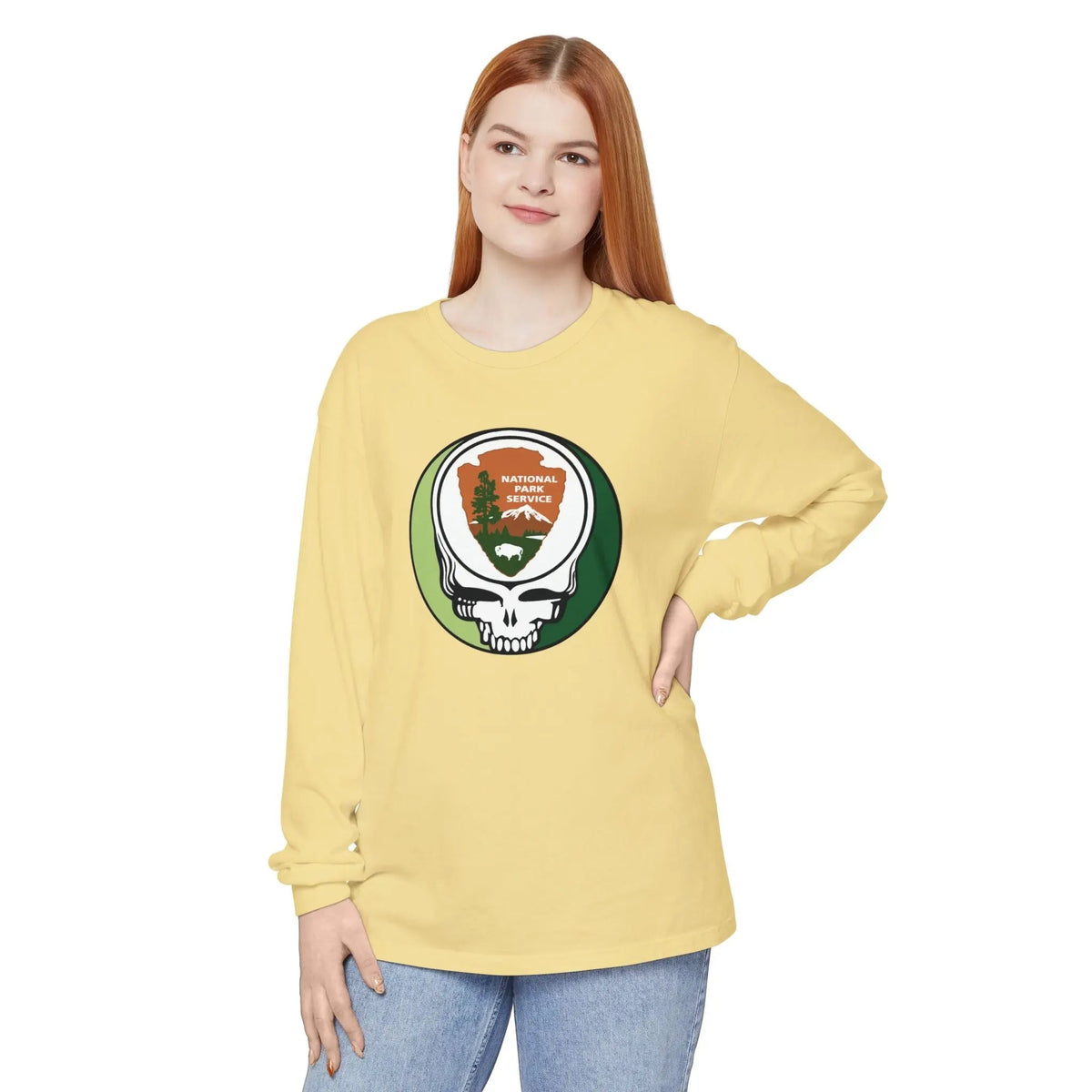 A woman modeling a pale yellow long-sleeve t-shirt with a large Grateful Dead Steerneck Skull graphic on the chest, paired with blue jeans against a plain white background.